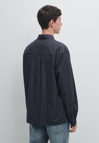 Zwart-grijs geruit overhemd met een kraag, lange mouwen en manchetten met knopen, met een ontspannen pasvorm en detail op het rugpand.