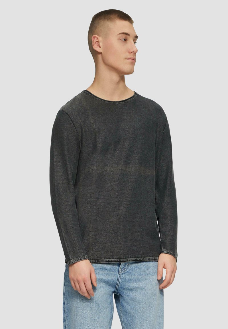 Zwart, gestructureerd shirt met lange mouwen en een ronde halslijn, met zichtbare stikdetails, gedragen over lichtblauwe jeans.