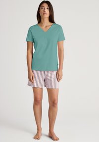 Teal T-shirt met korte mouwen en V-hals, gecombineerd met roze en witte gestreepte shorts. De stof lijkt zacht te zijn met een relaxte pasvorm en minimale ontwerpdetails.