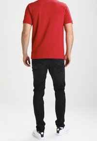 Camisa roja de manga corta, pantalones ajustados negros y zapatillas blancas con acentos verdes. Enfócate en la textura suave de la camisa y su diseño ajustado.