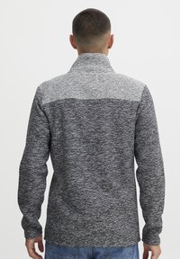 Fleece-Pullover mit hohem Kragen, der ein strukturiertes graues Muster, lange Ärmel und einen kontrastierenden hellgrauen oberen Abschnitt aufweist.