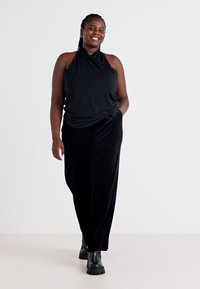 Top halter negro combinado con pantalones de pierna ancha negros, ambos con texturas suaves. El atuendo se complementa con botas negras hasta el tobillo.