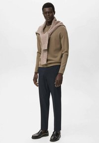 Pull en maille marron sur un col roulé taupe, associé à un pantalon bleu marine foncé et des mocassins noirs. Le pull a une finition texturée.