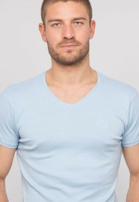 T-shirt bleu clair en V fabriqué en tissu doux, doté de manches courtes et d'un logo discret sur la poitrine. Design ajusté avec une texture lisse.