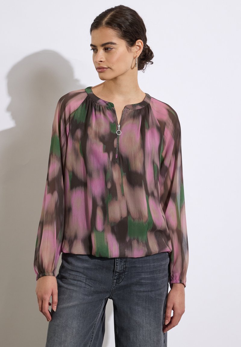 Gennemsigtig bluse med lange ærmer og lynlås i halsen. Har et mønster i lyserøde, grønne og brune nuancer. Letvægtsstoffet har en afslappet pasform.