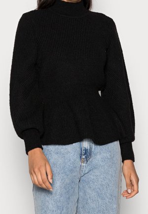 Czarny dziergany sweter z golfem, z bufkami na długich rękawach i dopasowaną talią, zestawiony z jasnoniebieskimi jeansami z wysokim stanem.