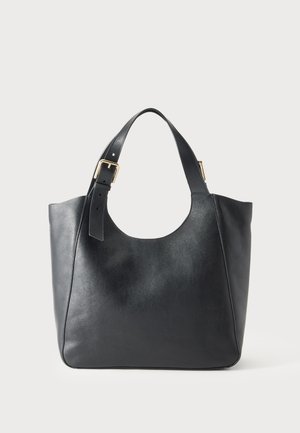 Sac cabas en cuir noir avec une large bandoulière réglable dotée d'une boucle dorée sur fond uni.