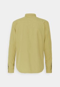 Camisa de manga larga, de color verde oliva claro, vista desde atrás con cuello recto y puños abotonados sobre un fondo blanco.