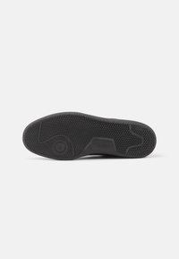 Black rubber shoe sole with textured grip pattern, featuring a circular accent and curved edges for flexibility.
