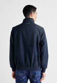Mornarska jakna na vjetar s visokim ovratnikom, elastičnim manžetama i rubom, izrađena od glatkog materijala; logo "PEPE JEANS" na leđima. Nosiva s trapericama.