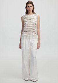 Top sin mangas de punto con un gran tejido abierto en gris claro, con un dobladillo acanalado. Combinado con pantalones blancos sueltos y texturizados y zapatos blancos.