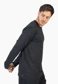 Langærmet sort t-shirt lavet af struktureret stof med en afslappet pasform, der har en rund halsudskæring og ingen synlige mønstre eller hardware.