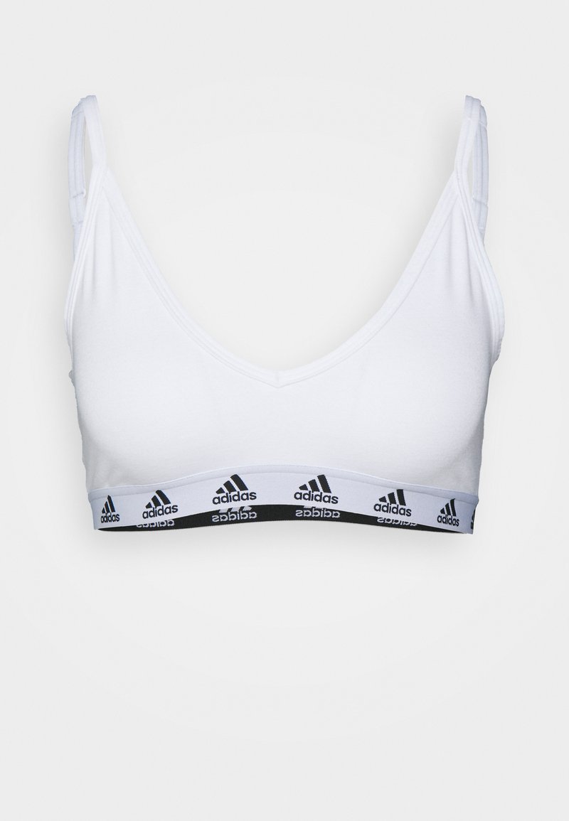 Bela športna modrčka z globokim V-izrezom, ki ima črn elastični trak okrašen z ponavljajočimi se belimi logotipi "adidas" ob dnu.