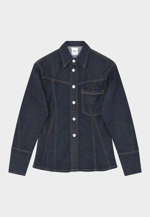 Chemise en jean bleu foncé à manches longues avec des boutons blancs, une poche poitrine, des coutures contrastées et un col structuré, posée à plat sur un fond blanc.