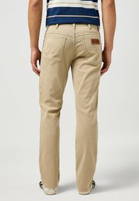 Pantaloni khaki con vestibilità dritta, dotati di tasche posteriori con dettagli di cucitura a triangolo e una patch in pelle marrone. Materiale in cotone, design casual.