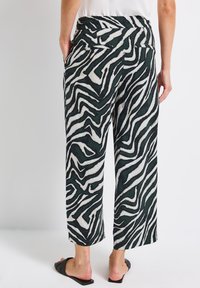 Schwarz-weiße, zebra-musterte, weit geschnittene Hose mit entspannter Passform, elastischem Bund und Taschen an den Hüften, kombiniert mit offenen Sandalen.