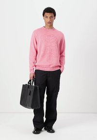 Rosa strikkegenser med blomsterdesign, rund hals, ribbestrikkede mansjetter, sammen med svarte cargo-bukser og en strukturert svart tote-veske.