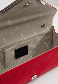 Clutch in suede rosso con una texture liscia, dotato di un interno foderato beige con Branding stampato e una patch logo nera. Chiusura a scatto in argento.