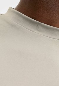 Lys beige, tekstureret stof med et tætsiddende halsdesign. Glat overflade og subtil glans, der fremhæver materialets stræk og fleksibilitet.