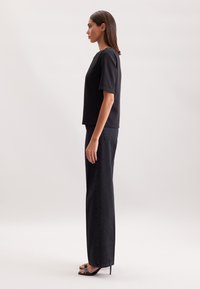 Top corto nero a maniche corte abbinato a jeans scuri a vita alta e a gamba larga. Tessuto morbido, design minimalista; il modello indossa tacchi neri con cinturini.