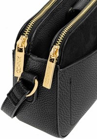Czarna skórzana torba o teksturowanej powierzchni, z dwoma złotymi zamkami błyskawicznymi i dopasowanym paskiem. Wnętrze wyłożone miękkim, ciemnym materiałem.