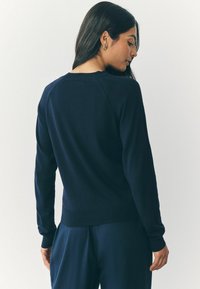 Marineblauwe gebreide trui met lange mouwen, ribgebreide boorden en een ronde hals. Gladde textuur, aansluitend op de heup, gedragen met bijpassende broek.