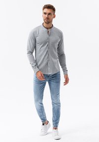 Camisa gris de manga larga con cuello henley, que cuenta con botones en la parte delantera. Se lleva con jeans de color azul claro y zapatillas blancas.