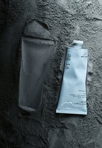 Ljusblå aluminiumtub med handkräm ligger på en mörkgrå, pudrig yta, med minimalistisk svart text och ett vitt skruvlock.