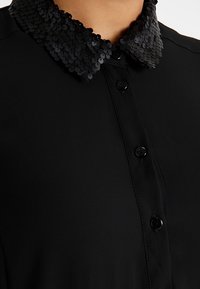 Zwarte blouse met een glinsterende kraag, gladde stof, sluiting met knopen aan de voorkant en een klassieke, getailleerde pasvorm.