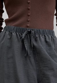 Pantalon à taille élastique avec cordon noué, porté avec un haut en maille côtelée marron avec des boutons recouverts de tissu sur le devant.