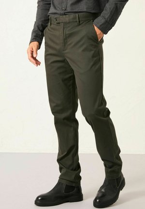 Olive green tailored pants with a flat front, side pockets, and belt loops. Paired with black ankle boots for contrast.