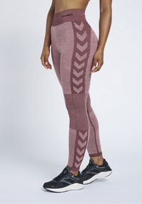 Burgundowe legginsy sportowe z teksturowanym wzorem, z bocznym panelem w wzór chevron. Połączone z czarnymi butami sportowymi.