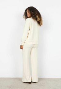 Set de haine lejere de culoare crem, cu mâneci lungi și pantaloni cu picioare largi. Țesătură moale, croială lejeră și detalii subtile în zona taliei.