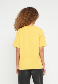 Kollane liibuva l�õikega T-särk lühikeste varrukatega, ümar kaelusega, pehmest kangast, ühevärvilise disainiga ja lõdva istuvusega.