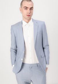 Sacou bleu deschis cu o cămașă albă dedesubt. Sacoul are o croială ajustată, rever ascuțit și închidere cu un singur nasture.