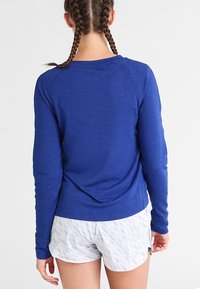Sudadera azul de manga larga con mangas raglán, escote redondo y un corte relajado, combinada con pantalones cortos blancos texturizados.