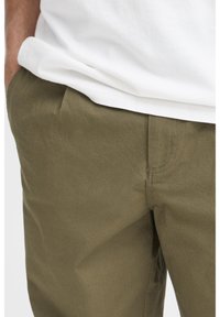 Khakibukser af struktureret stof med flad front og sidelomme, kombineret med en hvid t-shirt ved linningen.