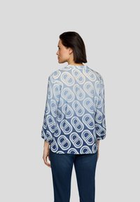 Langärmlige Bluse in einem blau-weißen geometrischen Muster, hergestellt aus einem leichten Stoff mit glatter Textur, mit einem runden Ausschnitt.