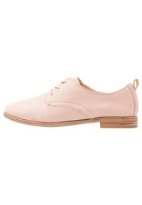 Chaussure oxford en cuir rose clair avec une texture lisse, bout arrondi, lacets et un talon en bois bas. Présente de fines rayures sur le dessus.