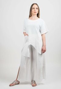 Robe longue en lin blanc, à manches courtes et ourlet asymétrique, dotée d'une poche latérale. La modèle porte des sandales argentées décoratives.