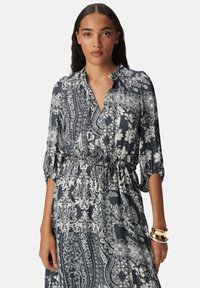 Abito a stampa floreale in blu navy e bianco, con colletto, maniche 3/4, vita elastica e tessuto leggero che crea un effetto fluido.