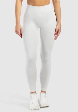 Witte high-waisted leggings met ribbeltextuur, aansluitend ontwerp en gladde stof. Gecombineerd met witte sportschoenen.