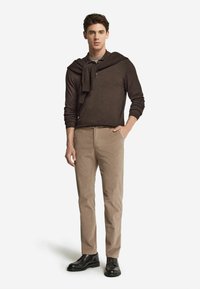 Brązowy dziany sweter noszony na szarej koszuli z kołnierzykiem. Kibellowe spodnie z korduroyu w kolorze jasnobeżowym i czarne buty na sznurowadła. Prosty, klasyczny design z luźnym krojem.