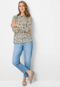 Lange mouwen, blouse met patroon in crème, marineblauw en geel met een ronde halslijn, gecombineerd met lichtblauwe rechte jeans en beige platte schoenen.