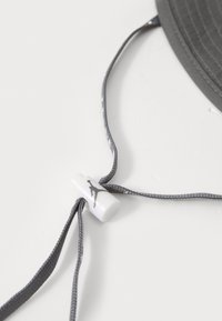 Gray cap with a textured surface and adjustable gray cords. Features a white plastic toggle with a black logo.