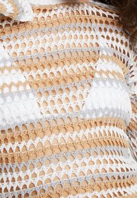 Haut en crochet avec un motif en maille ouverte en rayures blanches, grises et beiges, présentant une finition texturée et des formes hexagonales irrégulières.