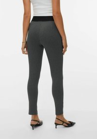 Leggings gris oscuro con rayas verticales, banda elástica alta y ajuste hasta el tobillo. Llevados con zapatos de tacón negros.