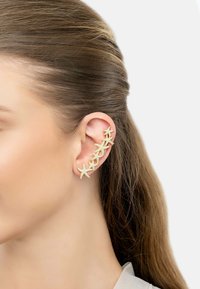 Gold starfish ear cuff with textured surface, extending along the ear. Features eight starfish linked together, set against light-colored skin.
