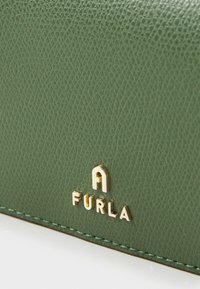Green textured leather wallet featuring a prominent gold logo "FURLA" and contrasting stitching along the edges.