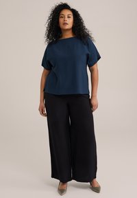 Top azul marino de manga corta con escote barco, combinado con pantalones negros de pierna ancha. Textura lisa con un ligero brillo y aberturas laterales.